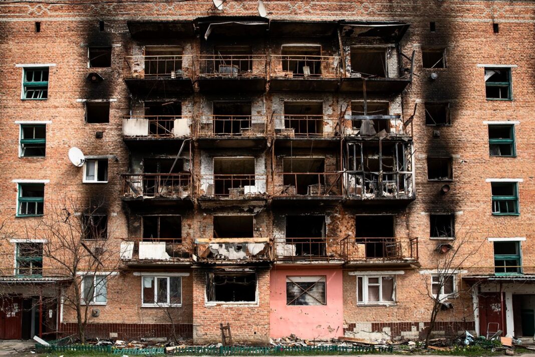 Фасад багатоповерхового житлового будинку з пошкодженими та обгорілими внаслідок бойових дій балконами.